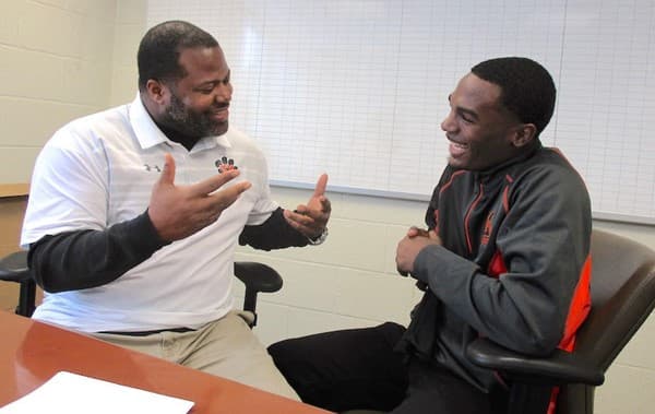 Two men sit in an office, laughing and talking with expressive hand gestures.