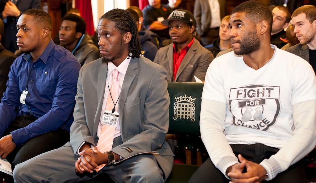 Three men sit in a row, one wearing a suit and another a slogan t-shirt.